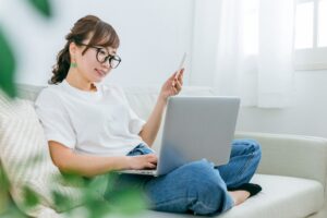 ノートパソコンとスマホをソファーの座って見る女性